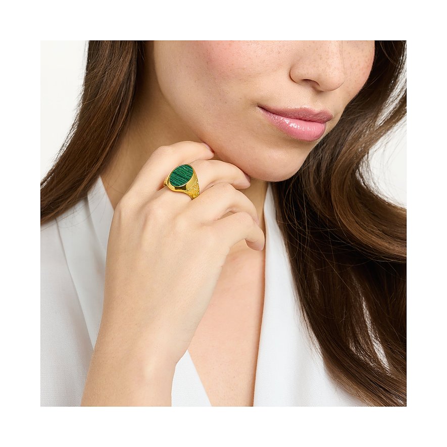 Ein Damenring von Thomas Sabo aus vergoldetem Silber mit einem ovalen Malachit Farbstein sitzt am Finger einer Frau.