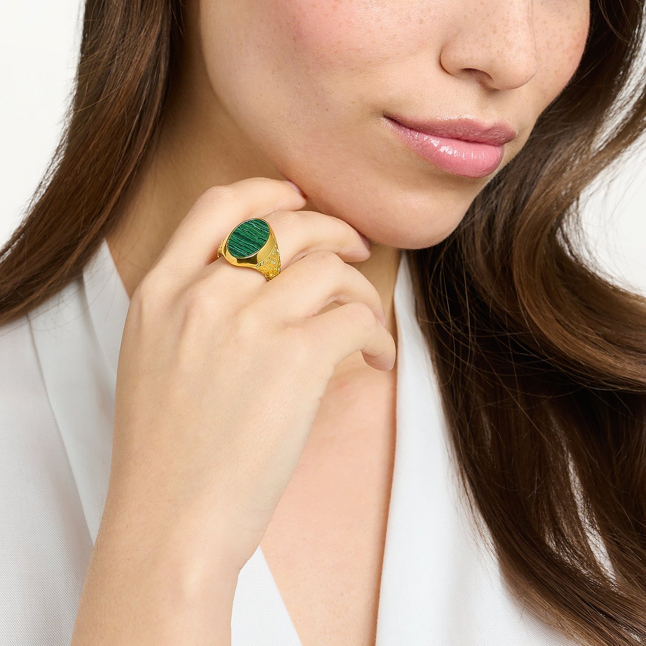 Ein Damenring von Thomas Sabo aus vergoldetem Silber mit einem ovalen Malachit Farbstein sitzt am Finger einer Frau.