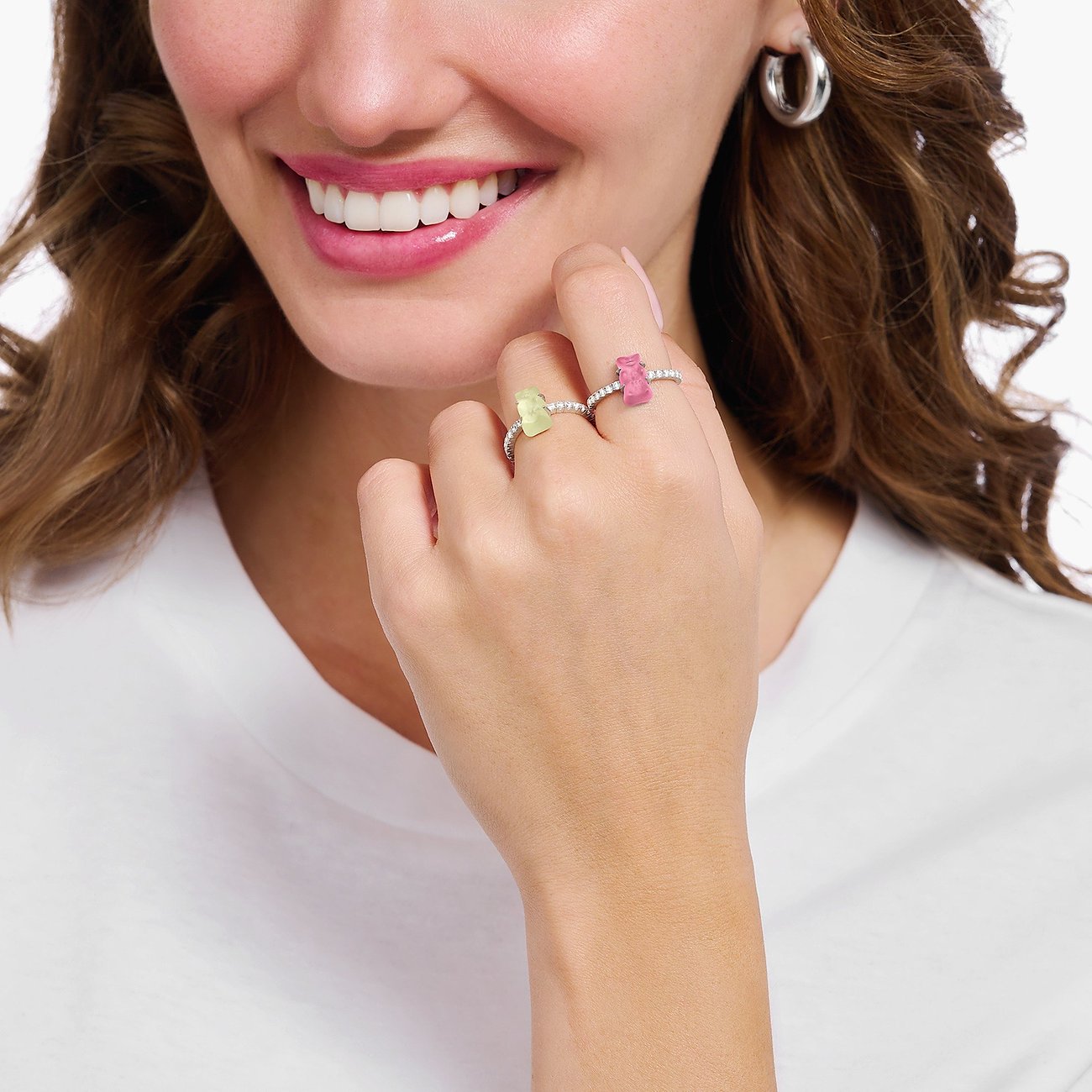 Nahaufnahme einer lächelnden Frau, die zwei Thomas Sabo Ringe aus Silber mit Zirkonia-Farbsteinen trägt.