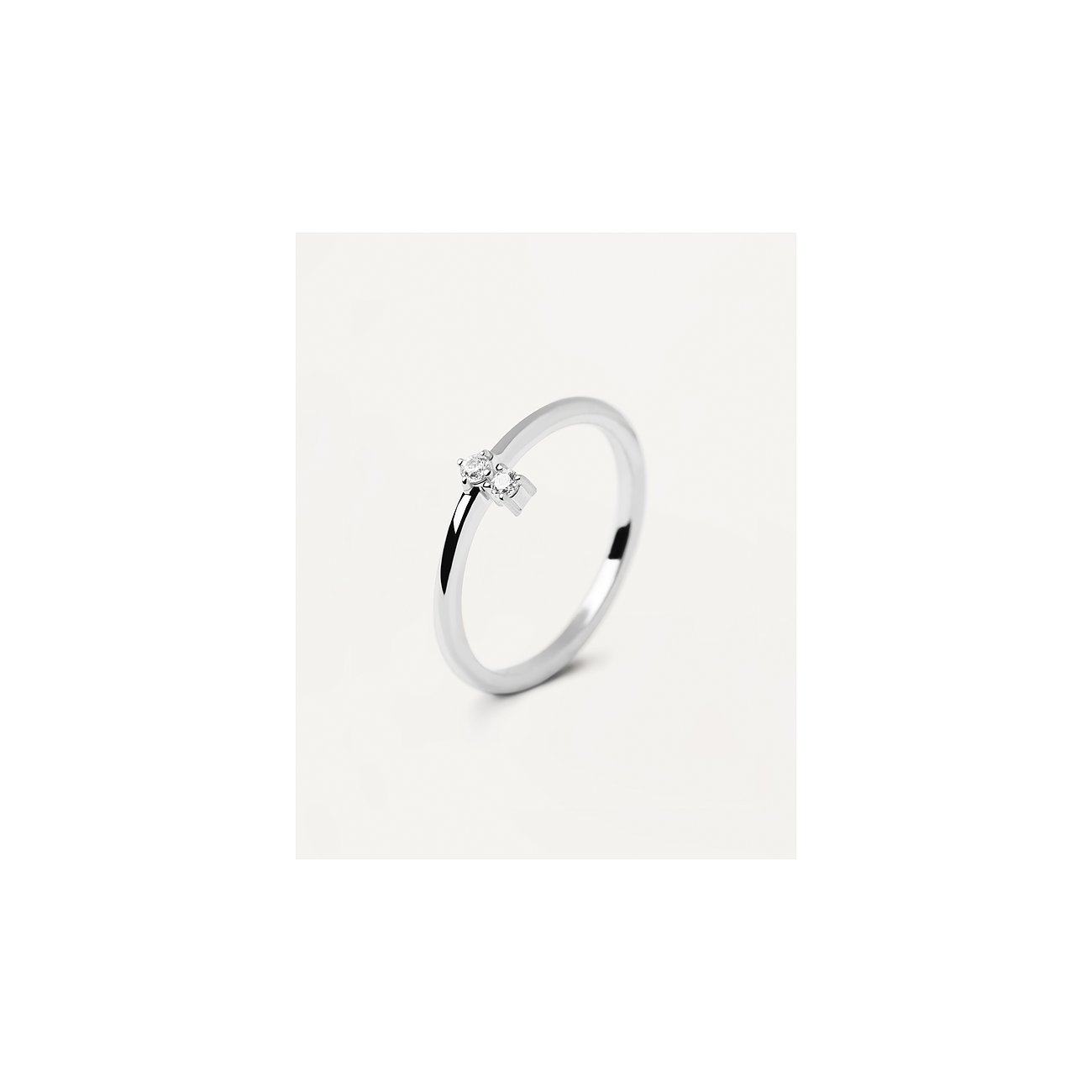 Zarter PdPaola Ring aus 925er Silber mit zwei kleinen, runden, leicht versetzten Zirkonia Farbsteinen auf weißem Hintergrund.
