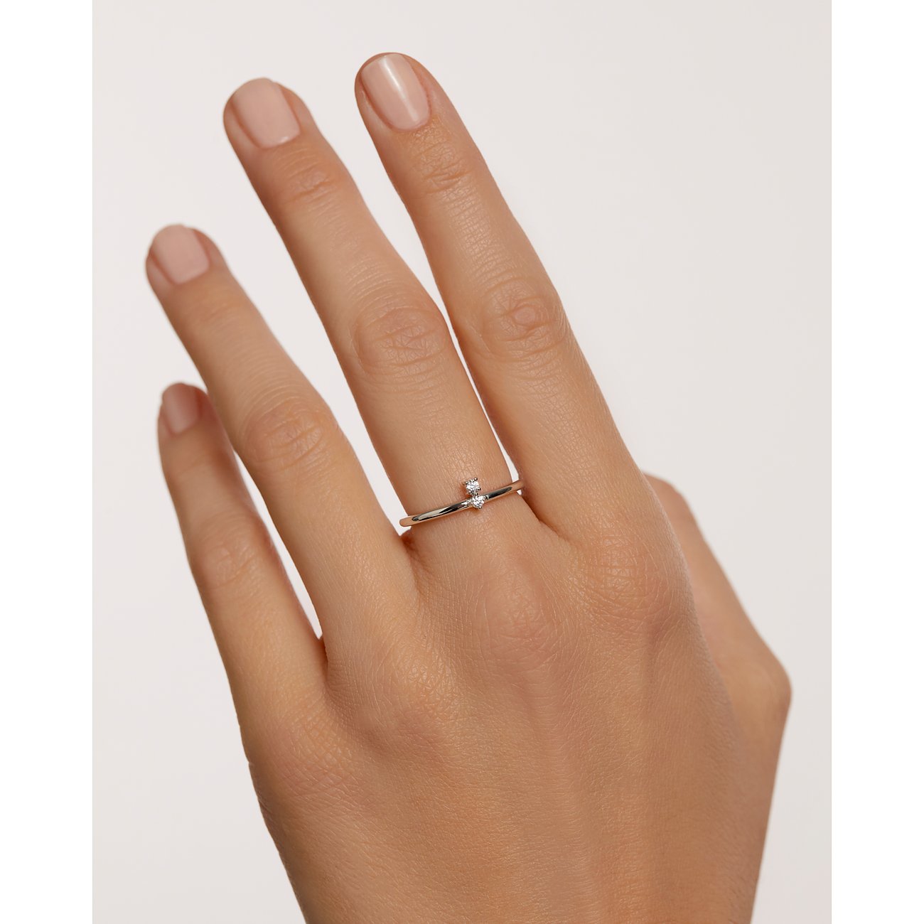 Ein zarter PdPaola Bandring aus Silber mit zwei kleinen, funkelnden Zirkonia-Farbsteinen, getragen an einem Finger.
