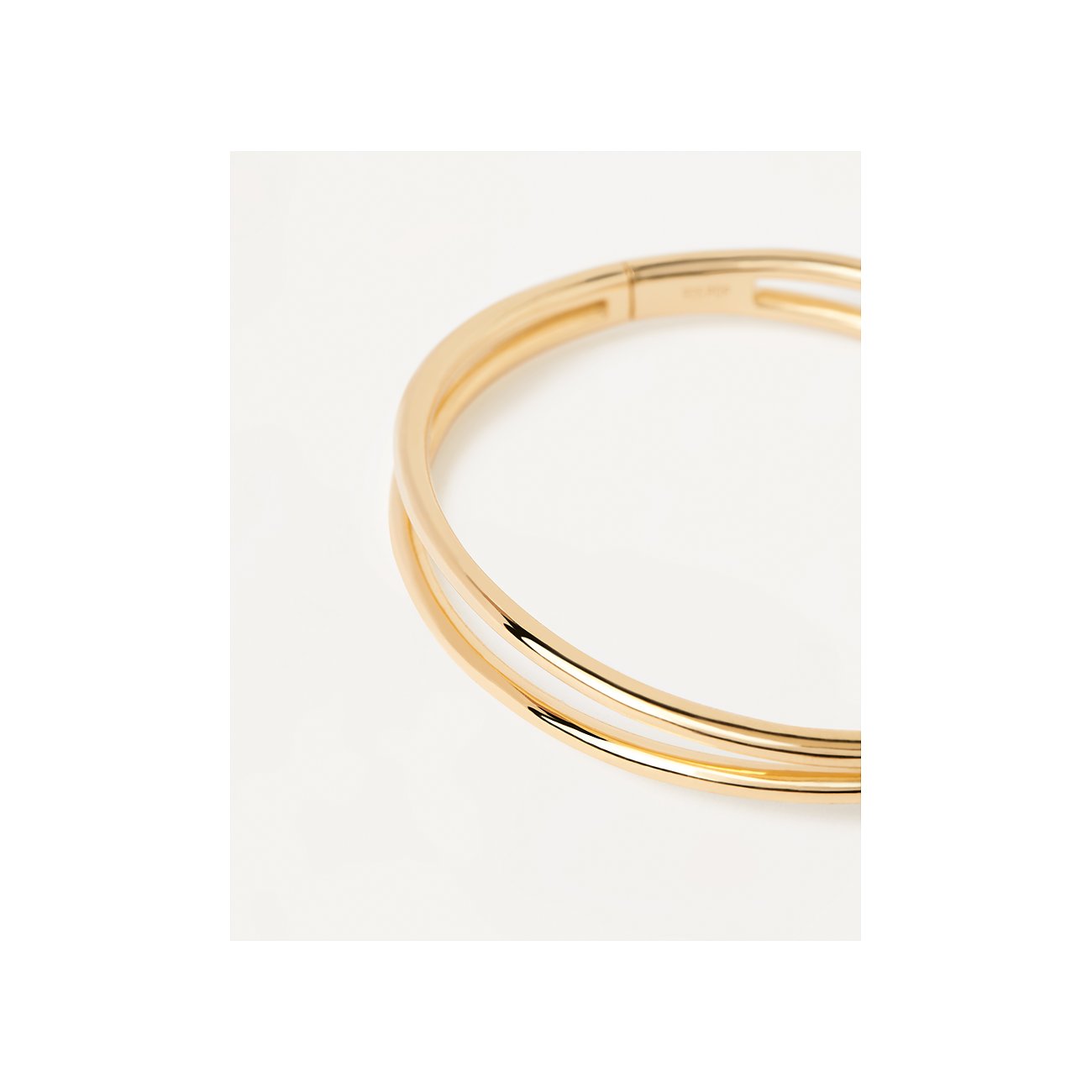 Närbild av ett gyllene PdPaola 925 sterlingsilverarmband med två eleganta, glänsande ringar.