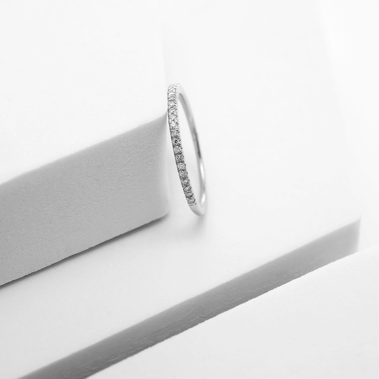 Weißgoldring, besetzt mit funkelnden Diamanten, der elegant auf einer stilisierten weißen Oberfläche liegt.