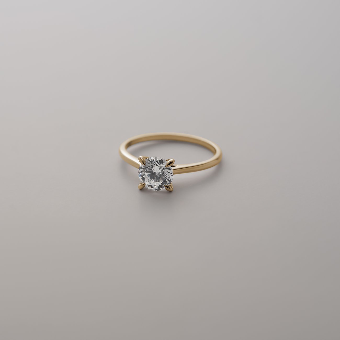 CHRIST Ring aus Gelbgold mit funkelndem Diamanten in Krappenfassung, auf glatter, grauer Oberfläche im Freisteller
