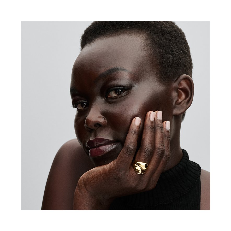 Eine Frau mit dunkler Haut und kurzen Haaren trägt einen goldfarbenen Pandora Metall-Ring am Ringfinger.