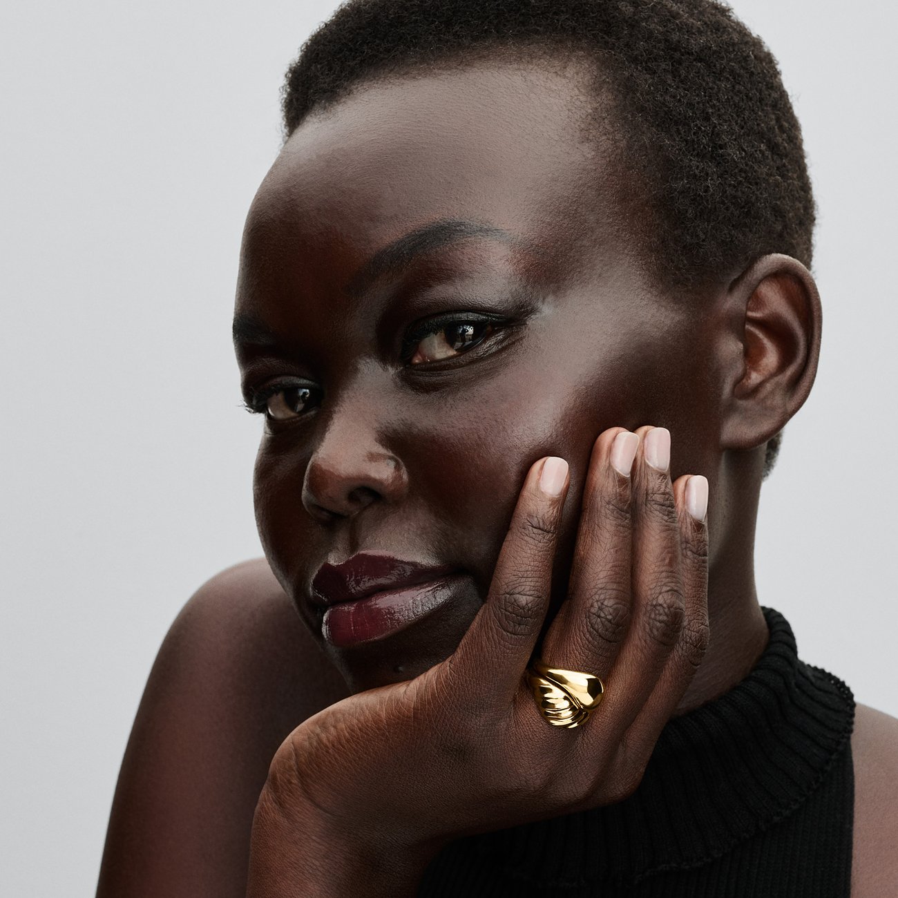 Eine Frau mit dunkler Haut und kurzen Haaren trägt einen goldfarbenen Pandora Metall-Ring am Ringfinger.