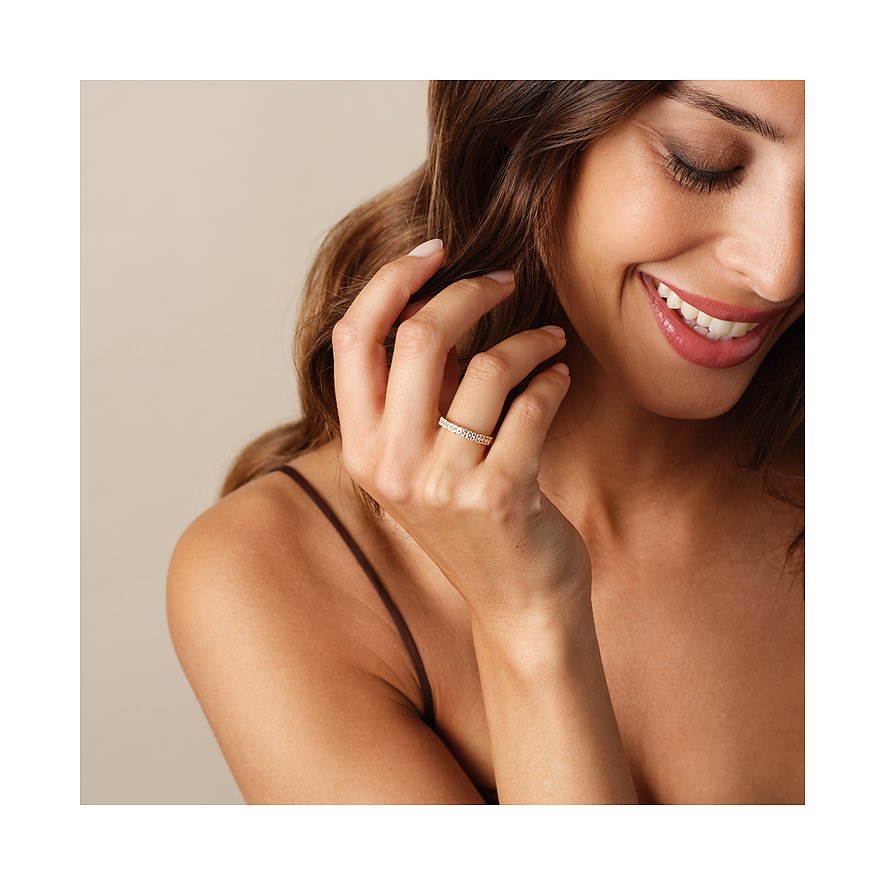 Närbild av leende kvinna med en CHRIST-ring i gult guld med diamanter, som stryker tillbaka sitt hår.