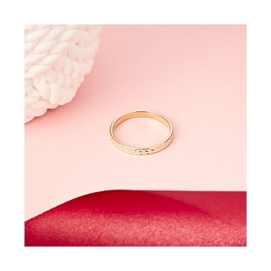 Een gouden CHRIST ring van gerecycled zilver met reliëfpatronen, liggend op roze en rode ondergrond.