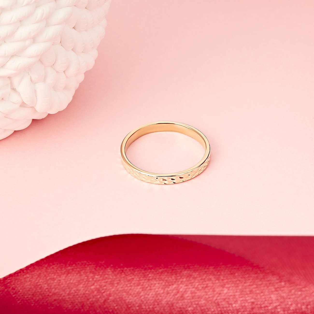 Een gouden CHRIST ring van gerecycled zilver met reliëfpatronen, liggend op roze en rode ondergrond.
