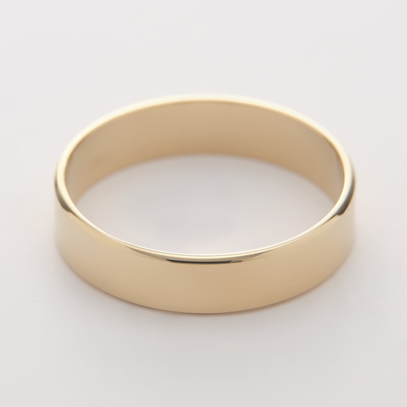 Nahaufnahme eines goldfarbenen, glänzenden CHRIST Bandrings in poliertem Gelbgold von oben links gesehen.