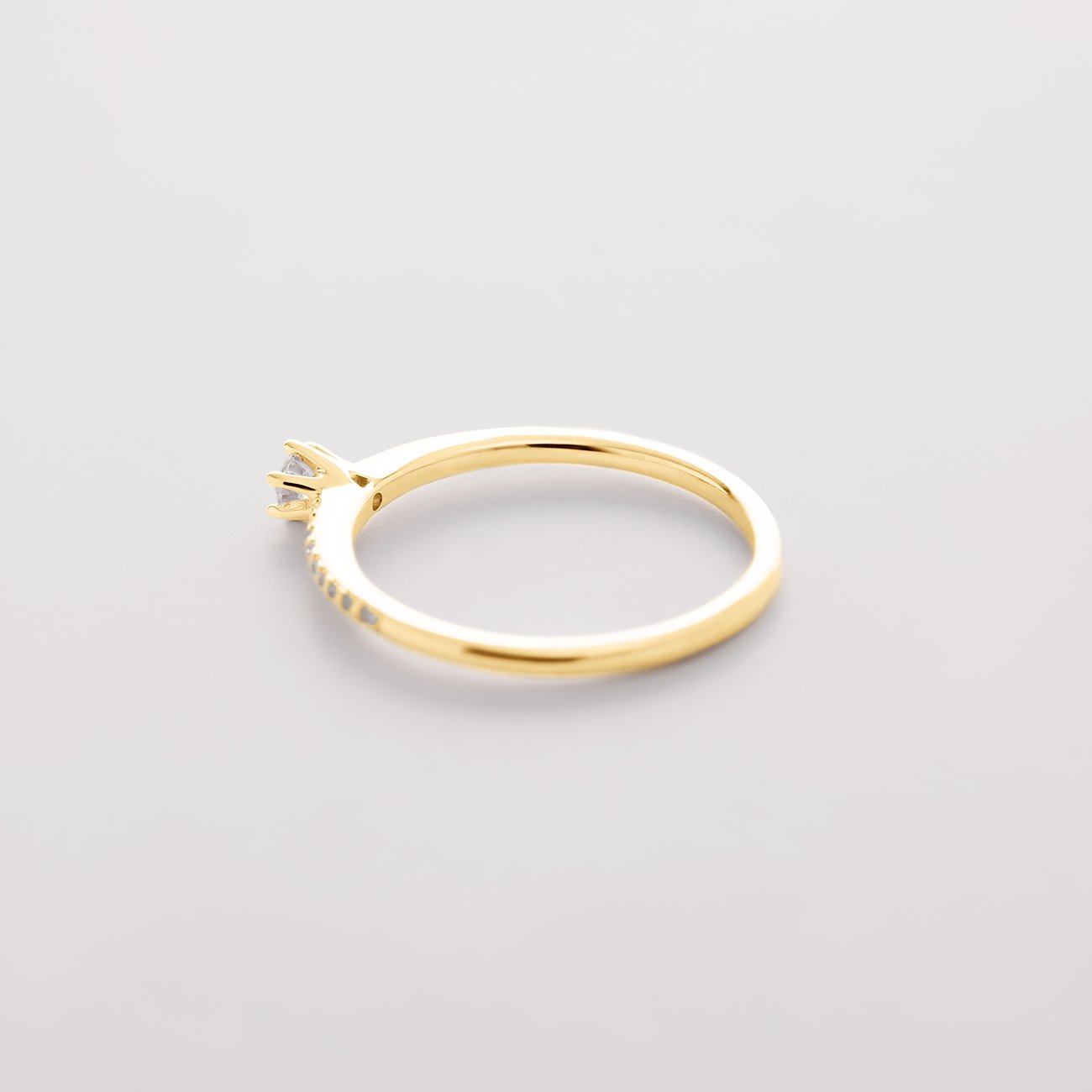 CHRIST Gelbgoldring mit einem einzelnen Diamanten und kleinen Diamanten auf der Ringschiene, von oben rechts gesehen.