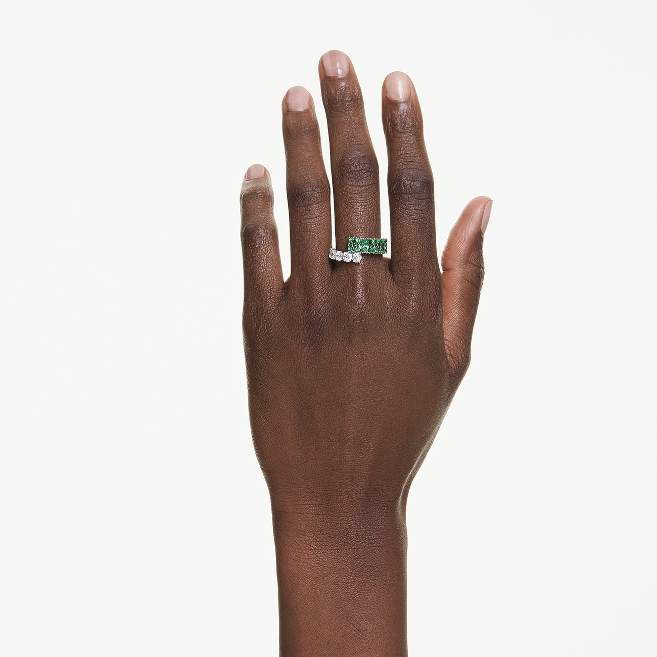 Hand trägt einen goldfarbenen Swarovski Ring mit quadratischen grünen Steinen und einen silberfarbenen Ring mit runden klaren Steinen.