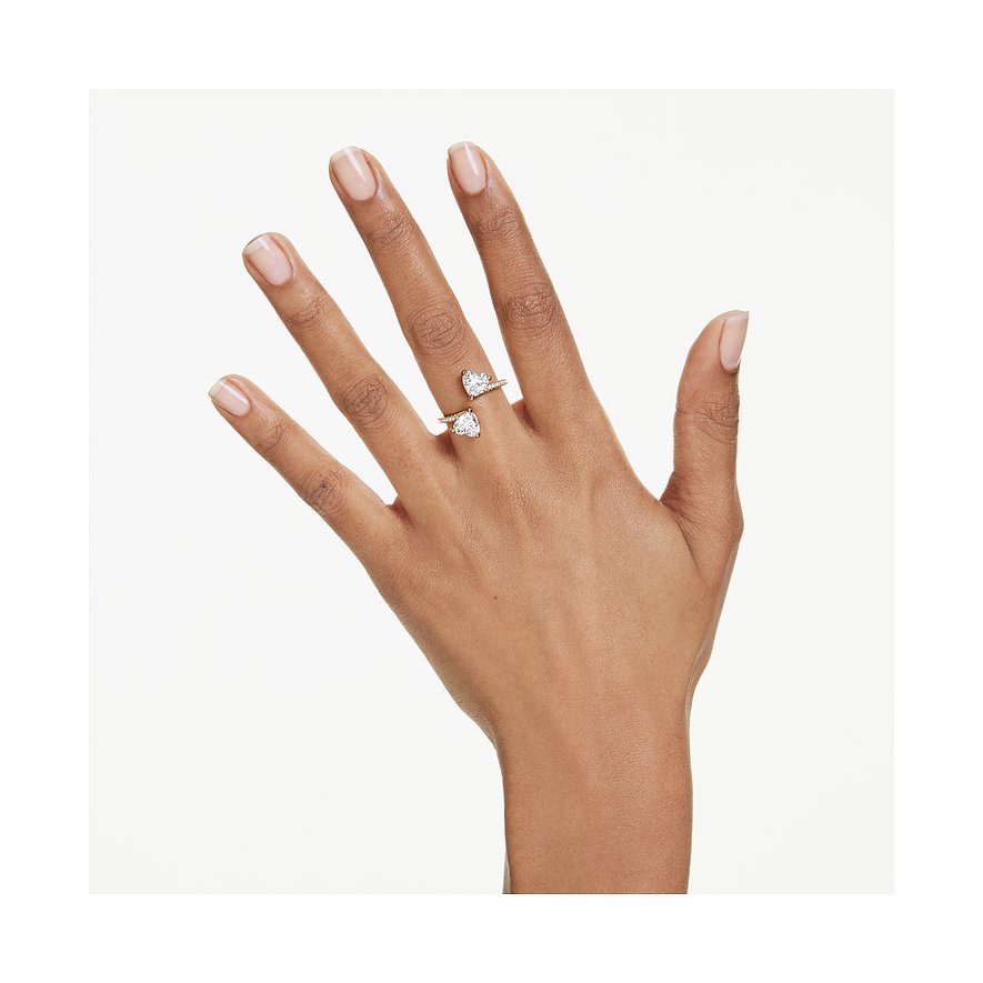 Een hand draagt een goudkleurige metalen Swarovski ring met twee hartvormige Swarovski kristallen.