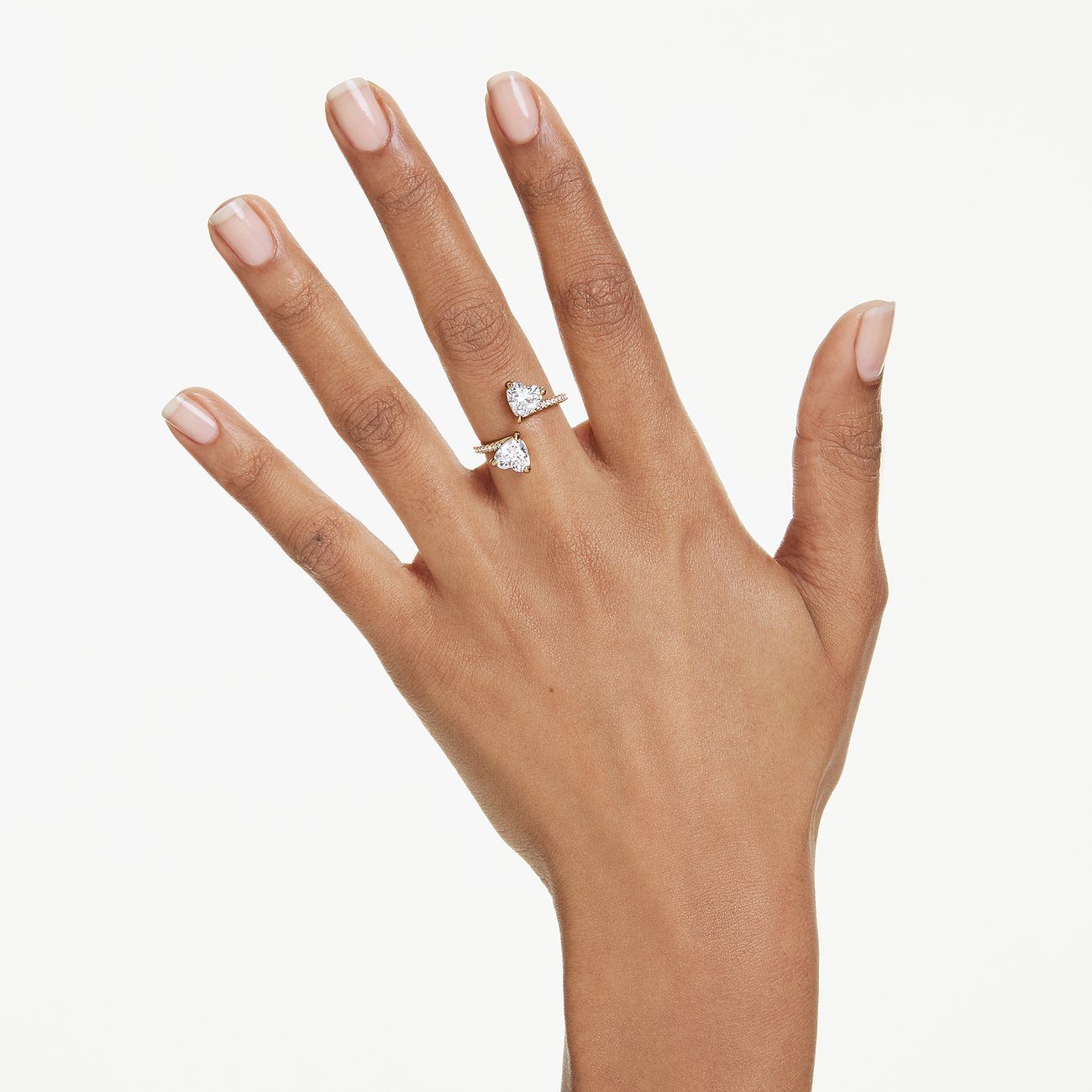 Een hand draagt een goudkleurige metalen Swarovski ring met twee hartvormige Swarovski kristallen.