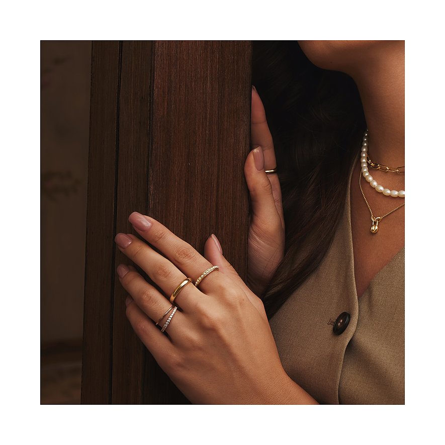 Vrouw draagt gouden Ania Haie ringen met heldere edelstenen en andere ringen. Ze draagt ook een parelketting.