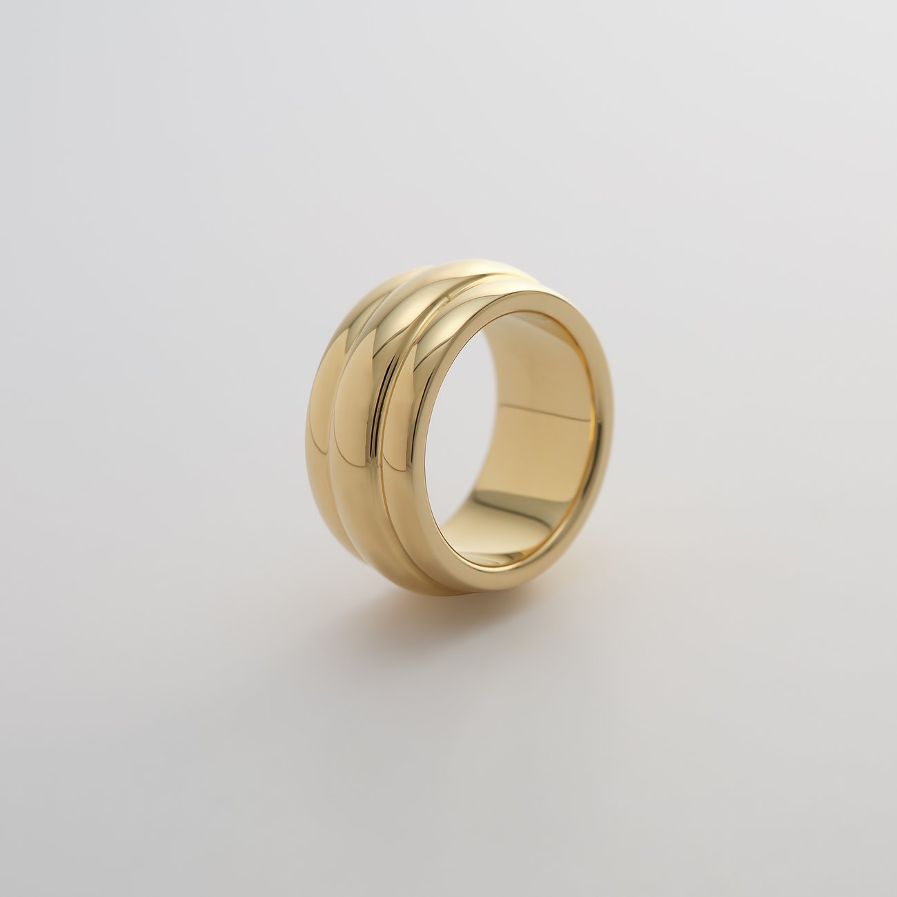 Ein glänzender, goldfarbener Guido Maria Kretschmer Ring aus Edelstahl mit geschwungenen Rillen, auf weißem Hintergrund.