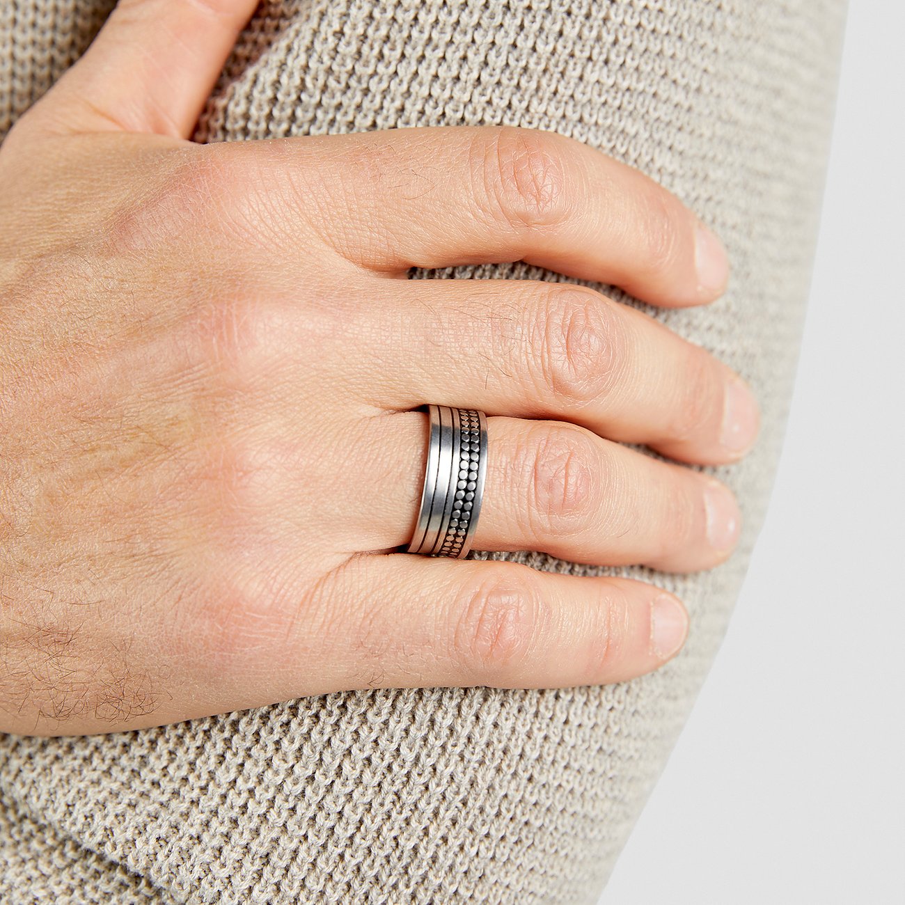 Nahaufnahme der Hand eines Mannes, die einen s.Oliver Ring aus breitem Edelstahlband und Zierperlen trägt.