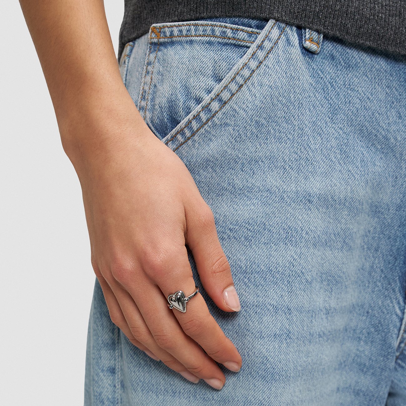 Gros plan d'une main portant une bague Liebeskind en acier inoxydable avec pendentif cœur à l'annulaire.
