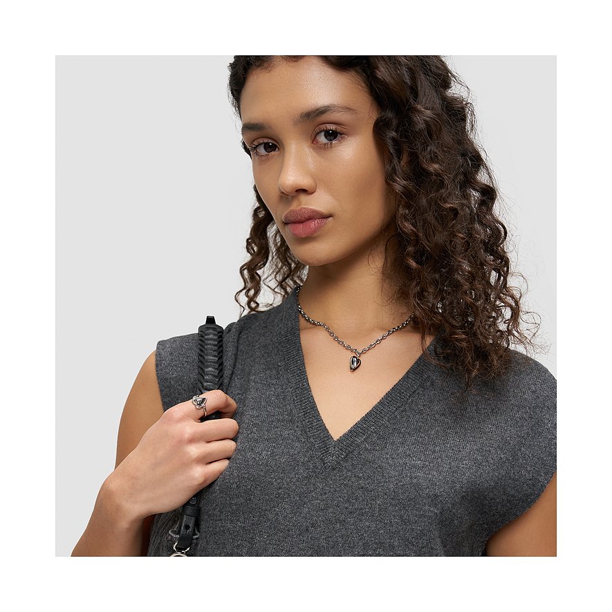 Le modèle porte une bague Liebeskind en acier inoxydable et un collier cœur sur un haut gris.
