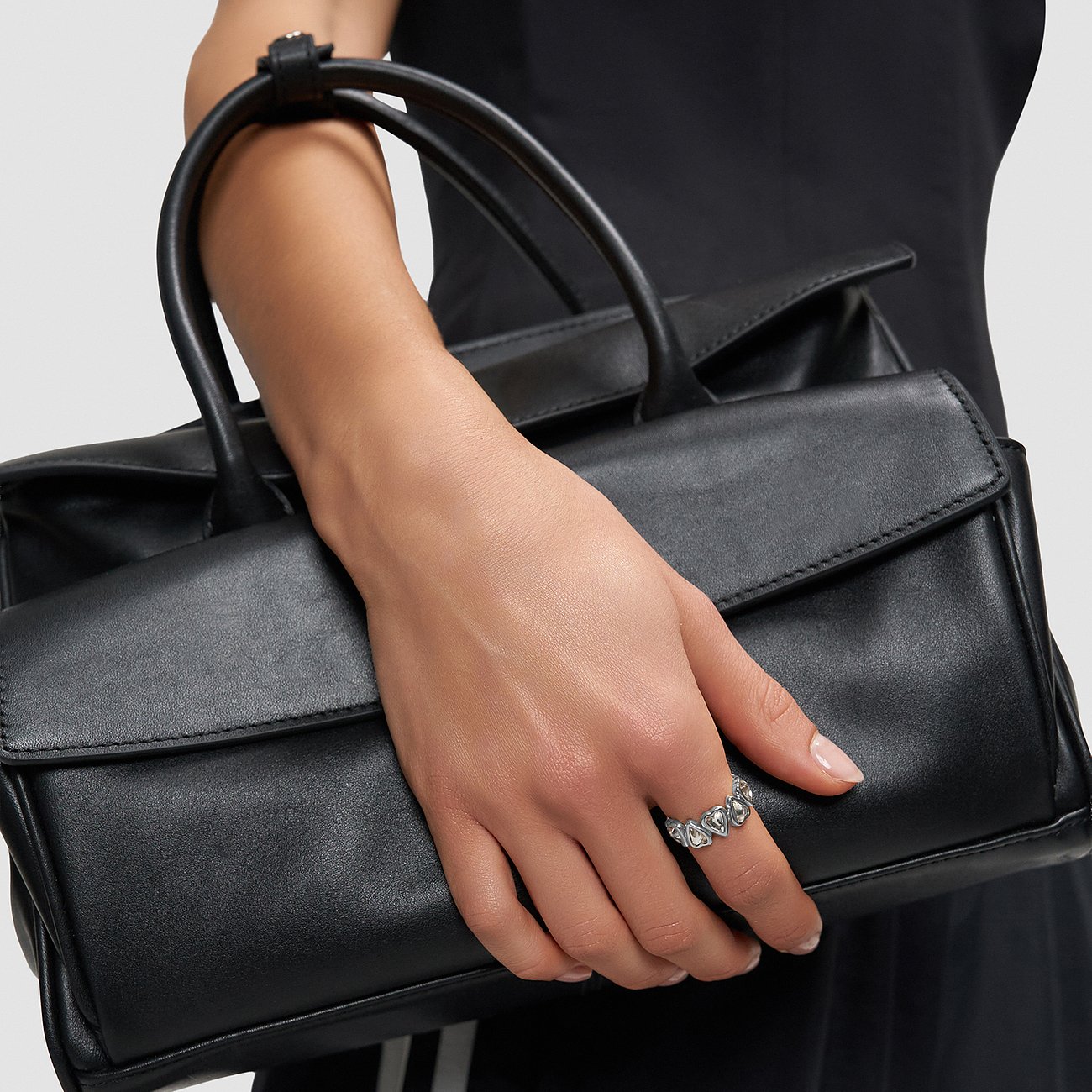 Une bague cœur en acier inoxydable Liebeskind sur une main tenant un sac à main noir.