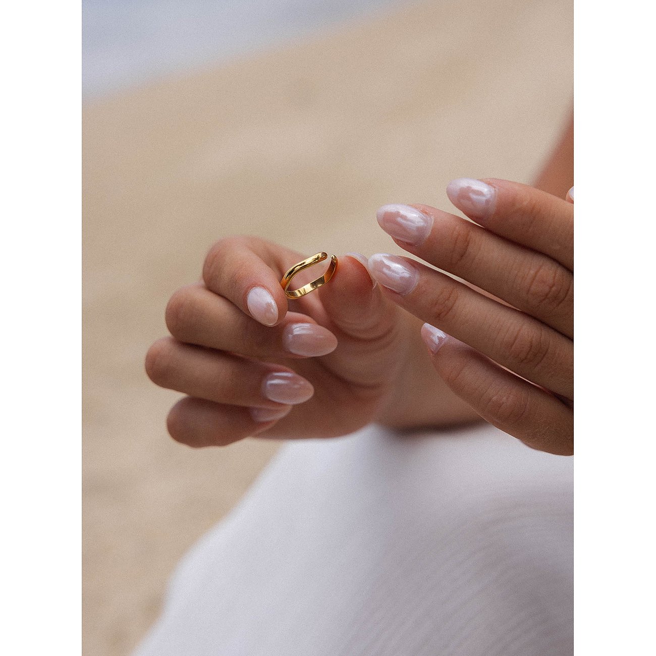 Vrouwenhanden houden een goudkleurige Purelei ring vast. De nagels van het model glanzen in een lichtroze tint.