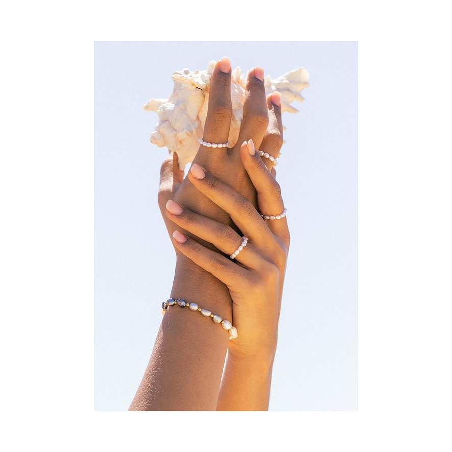 Twee handen houden een zeeschelp vast, versierd met meerdere ringen en een armband van Purelei parels.
