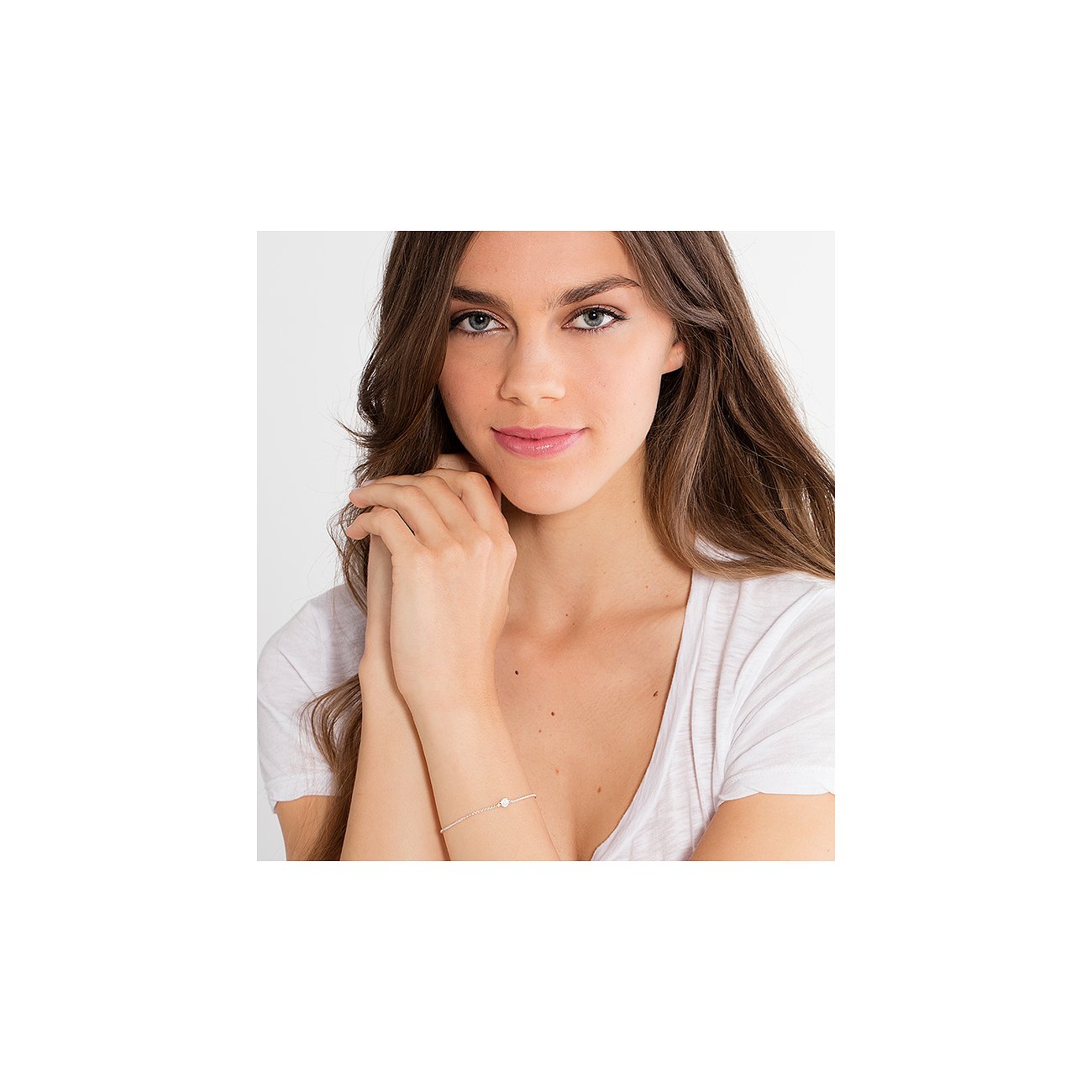 Frau trägt silbernes Thomas Sabo Armband mit Diamant und hellem Kettendesign. Haare offen, Hände am Kinn, weißes T-Shirt.
