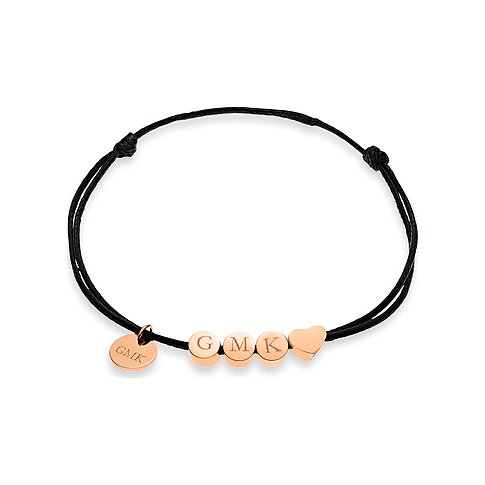 Ein Guido Maria Kretschmer Armband aus schwarzer Baumwolle und roségoldfarbenem Edelstahl. Es zeigt "GMK" und ein Herz.