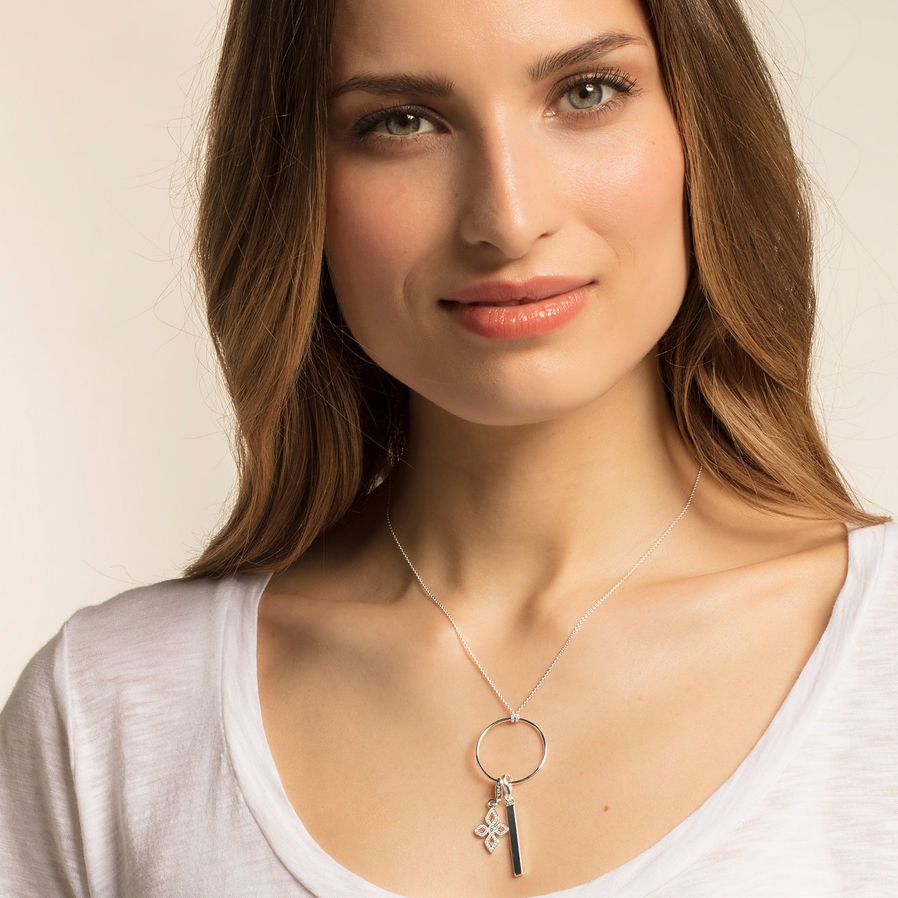 Model trägt Thomas Sabo Silberkette mit großem Ringanhänger, schwarzem Stabanhänger und kleinem floralen Anhänger.