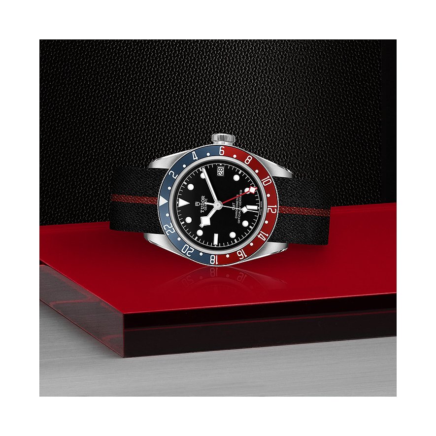 Tudor Herrenuhr mit Edelstahlgehäuse, schwarzem Zifferblatt und rot-blauer Lünette.