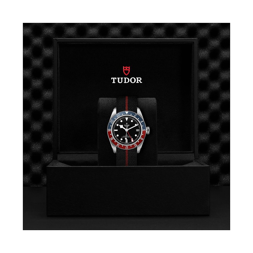 Tudor Herrenuhr mit Edelstahlgehäuse, schwarzem Zifferblatt und rot-blauer Lünette.