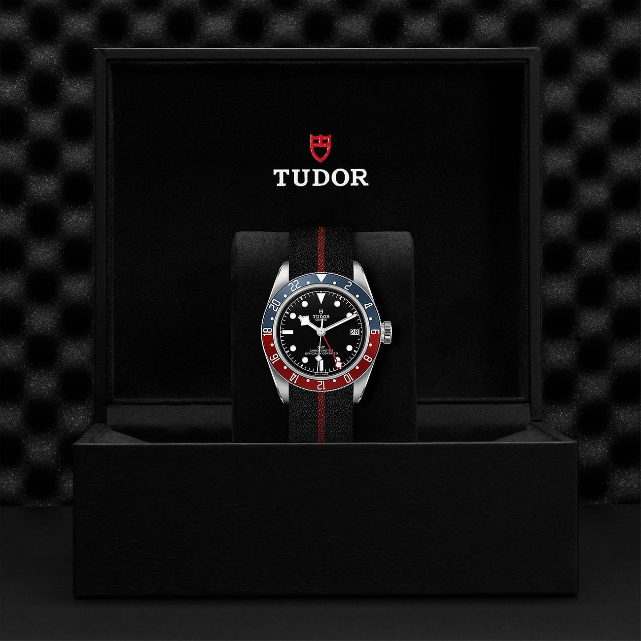 Tudor Herrenuhr mit Edelstahlgehäuse, schwarzem Zifferblatt und rot-blauer Lünette.