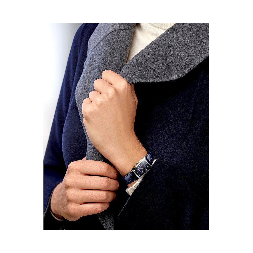 Eine Frau trägt eine rechteckige Longines Damenuhr aus Edelstahl mit marineblauem Lederarmband am Handgelenk.