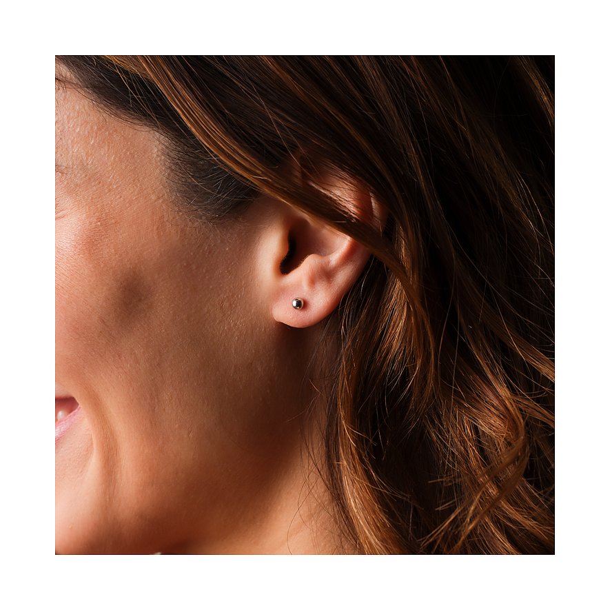 FAVS Ohrschmuck: Glänzender, runder Silberohrstecker, getragen am Ohr einer Frau mit braunen Haaren.