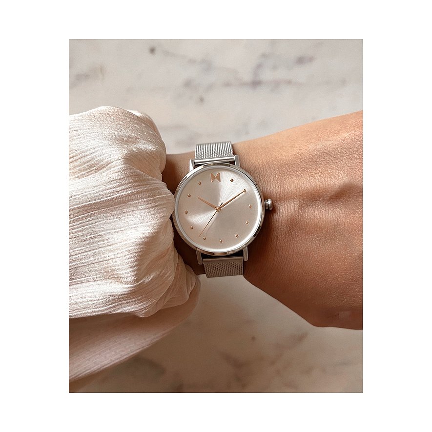 Eine MVMT Damenuhr aus Edelstahl mit rundem, milchigem Zifferblatt und silberfarbenem Milanaise-Armband am Handgelenk.