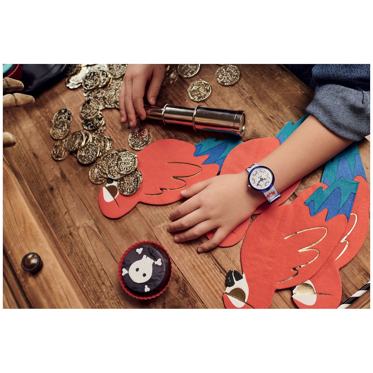 Ein Kind mit einer Flik Flak Kinder-/Jugenduhr aus Kunststoff bei Piratenspielen, umgeben von Goldmünzen.