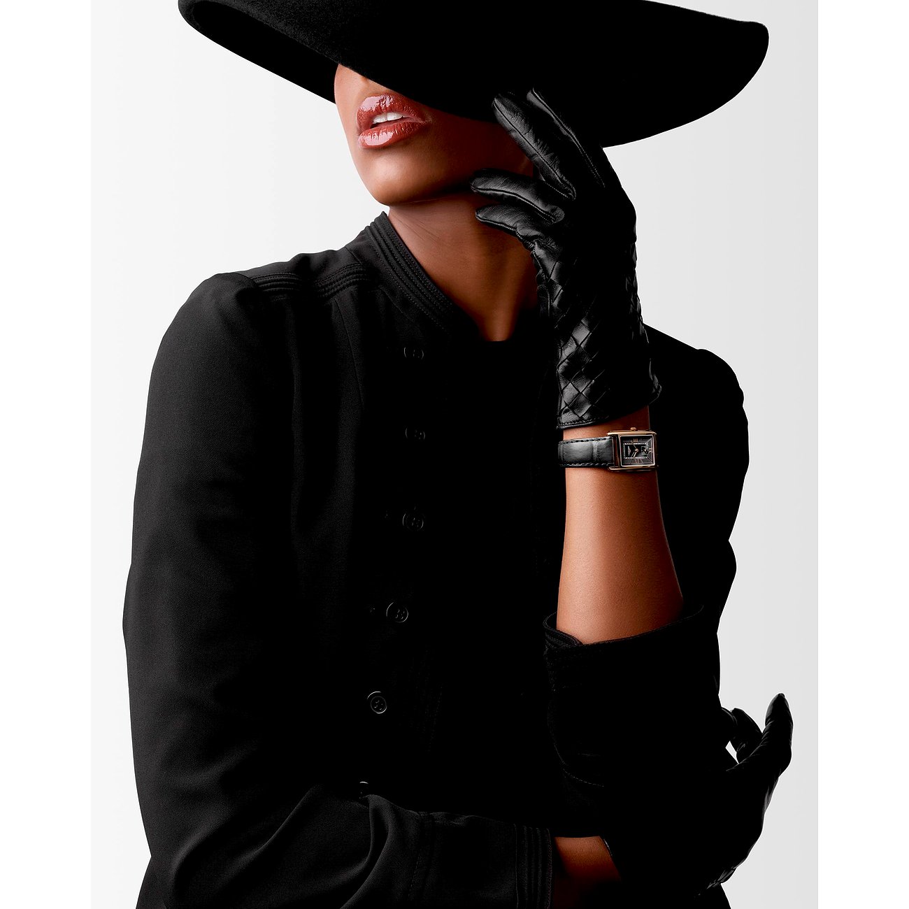 Nahaufnahme eines Models mit schwarzem Hut und Handschuhen, die eine Longines Damenuhr aus Roségold trägt.