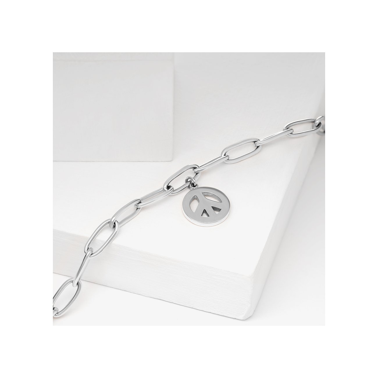 Guido Maria Kretschmer Armschmuck aus glänzendem Edelstahl mit langen, ovalen Gliedern und einem Peace-Zeichen-Anhänger.
