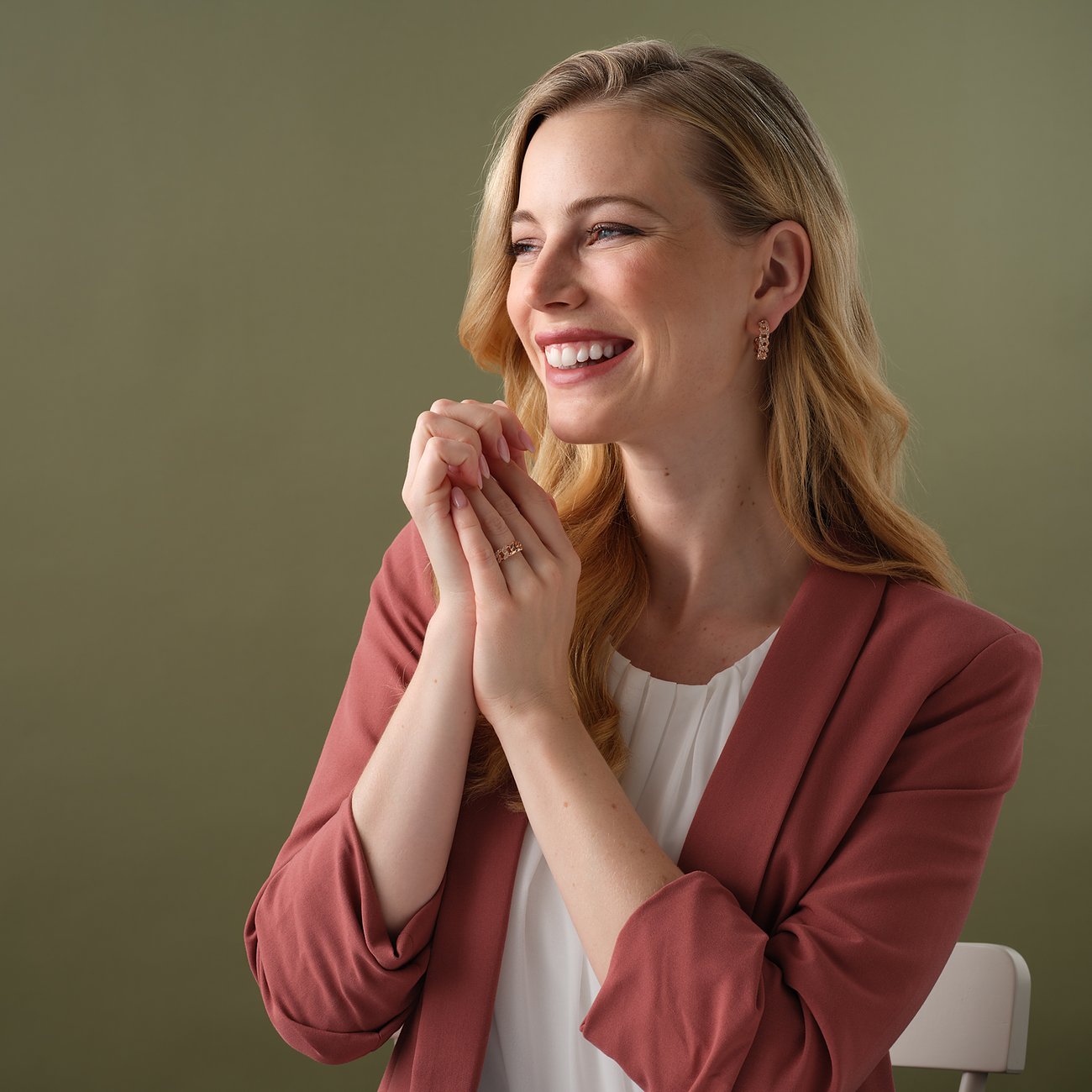 Närbild på en leende kvinna som bär guldfärgade JETTE silverörhängen med zirkonia och en matchande ring.