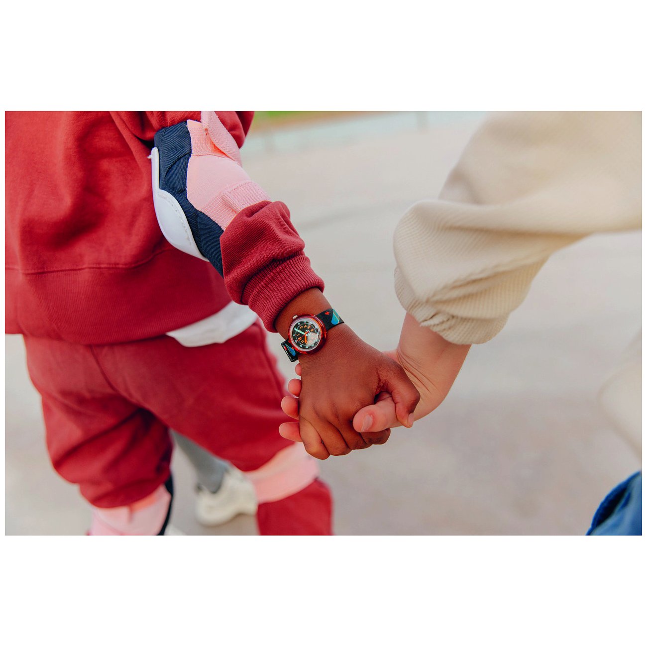 Närbild av två barn som håller hand. Ett bär en Flik Flak barn/ungdomsklocka i plast.
