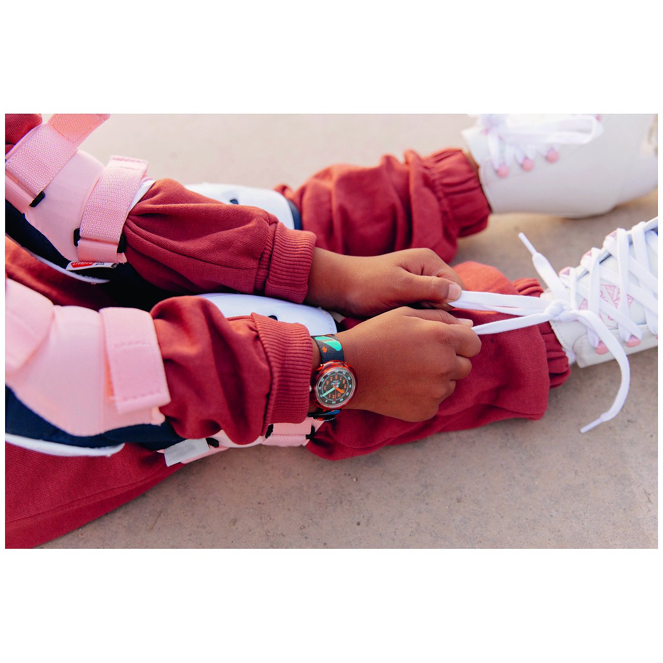 Närbild av en Flik Flak barnklocka i plast på handleden av ett barn som knyter skosnörena.