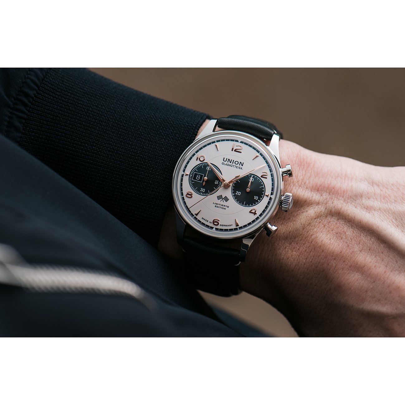 Union Glashütte Edelstahluhr am Handgelenk eines Mannes, helles Zifferblatt, Chronographenanzeigen, schwarzes Lederarmband.