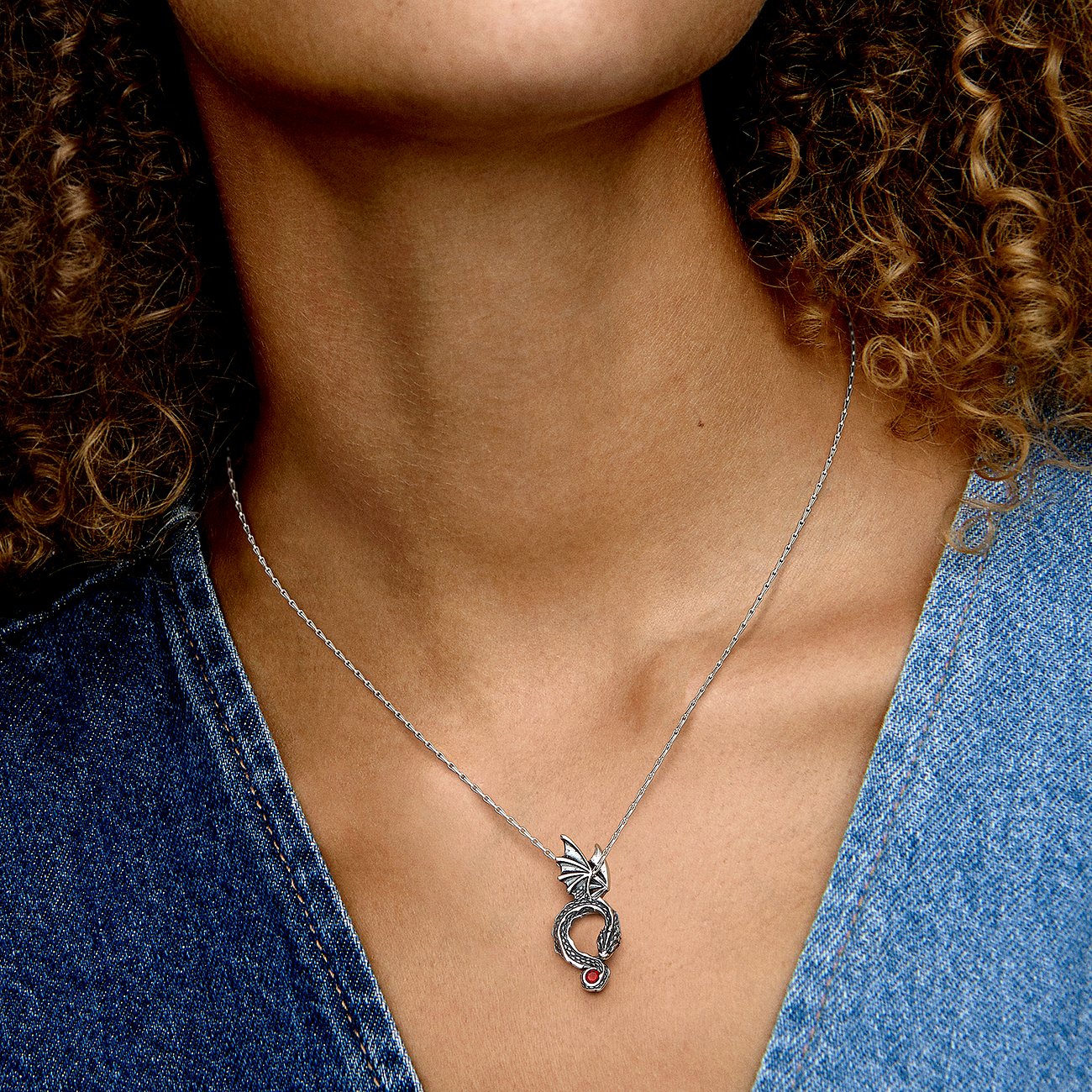 Eine Frau trägt eine Pandora Halskette aus 925er Silber mit einem Drachenanhänger und einem roten Kristall als Farbstein.