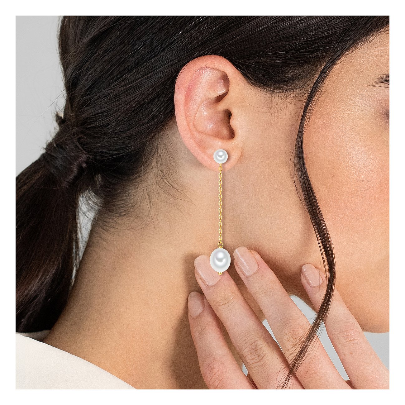 Valero Pearls Ohrschmuck: Eine Detailaufnahme zeigt einen langen goldfarbenen Ohrhänger mit zwei weißen Perlen.