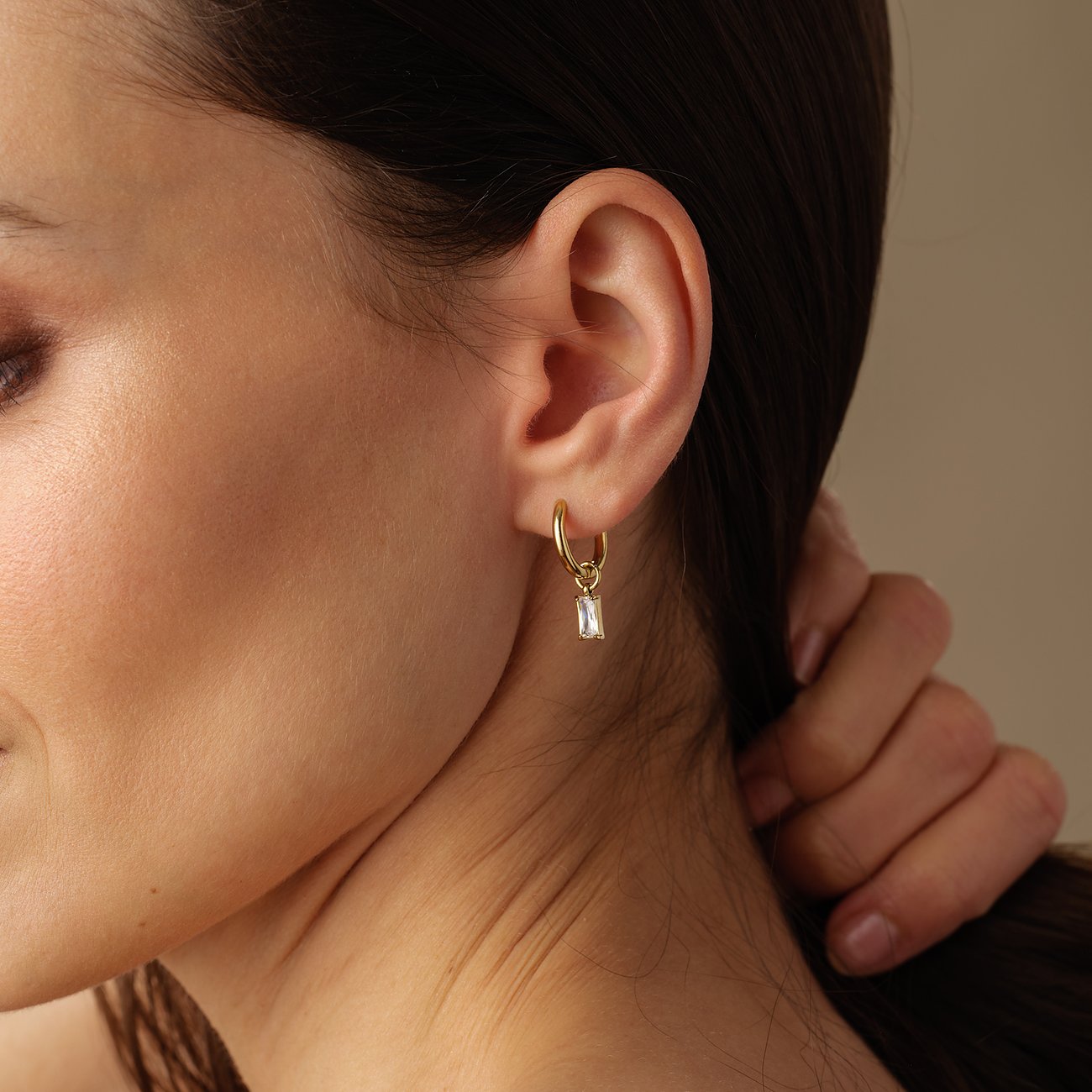 FAVS Ohrschmuck aus gelbvergoldetem Edelstahl mit hängendem Baguette-Zirkonia, getragen am Ohr einer Frau.