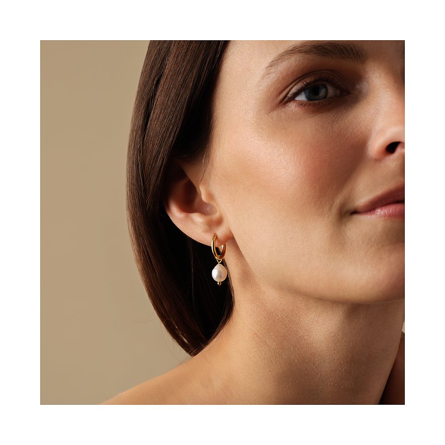 FAVS örhängen i rostfritt stål med pärlor. En kvinna bär den gyllene kreolörhänget med en stor vit pärla.