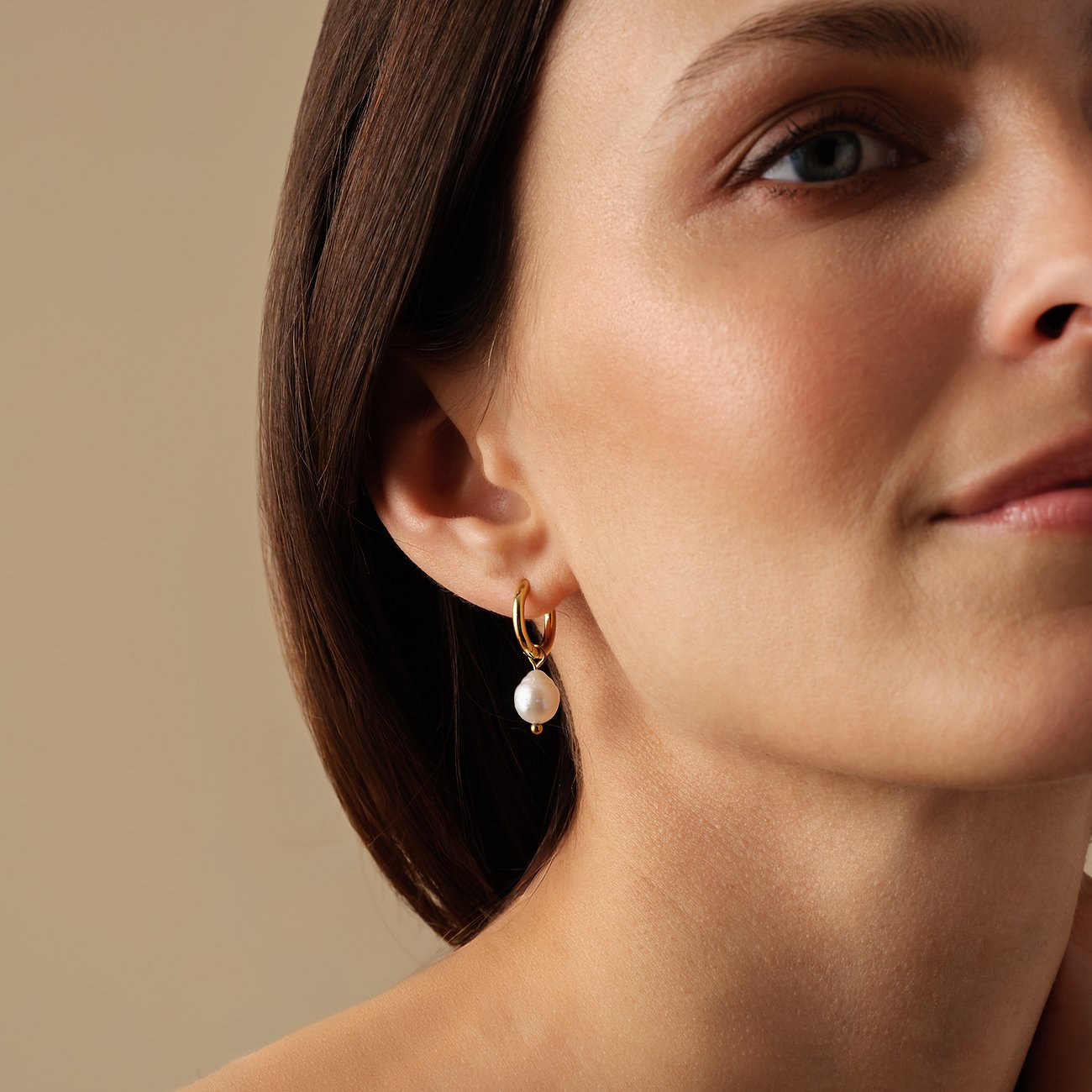 FAVS örhängen i rostfritt stål med pärlor. En kvinna bär den gyllene kreolörhänget med en stor vit pärla.