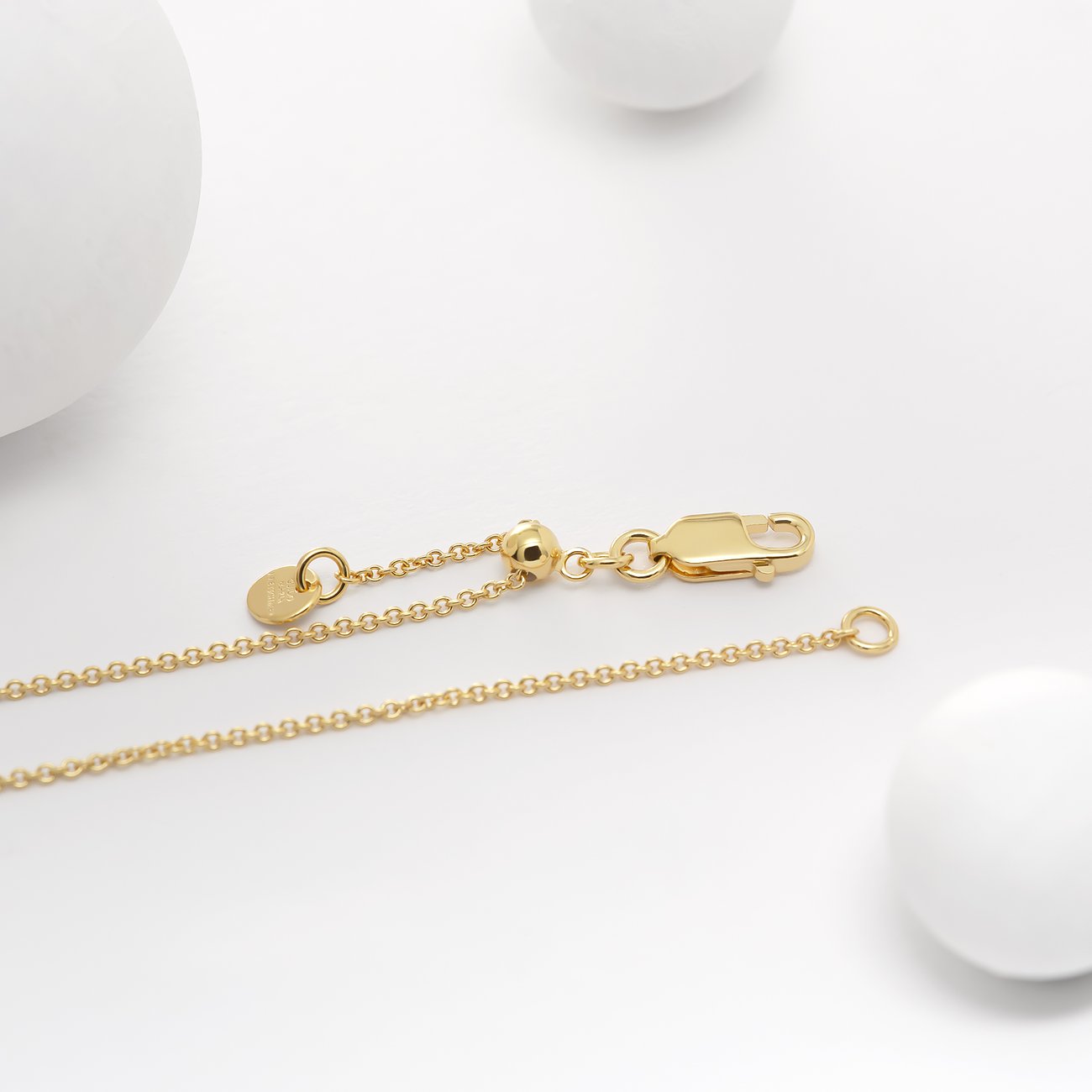 Detailansicht eines Guido Maria Kretschmer goldenen Silberarmbandes mit Karabinerverschluss, Verlängerungskette und Kugel.