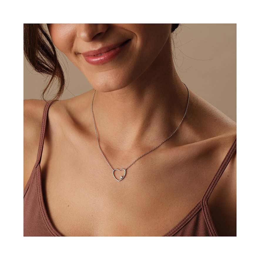 Een vrouw draagt een CHRIST ketting van gerecycled 925 zilver met hartvormige hanger en zirkonia als kleursteen.