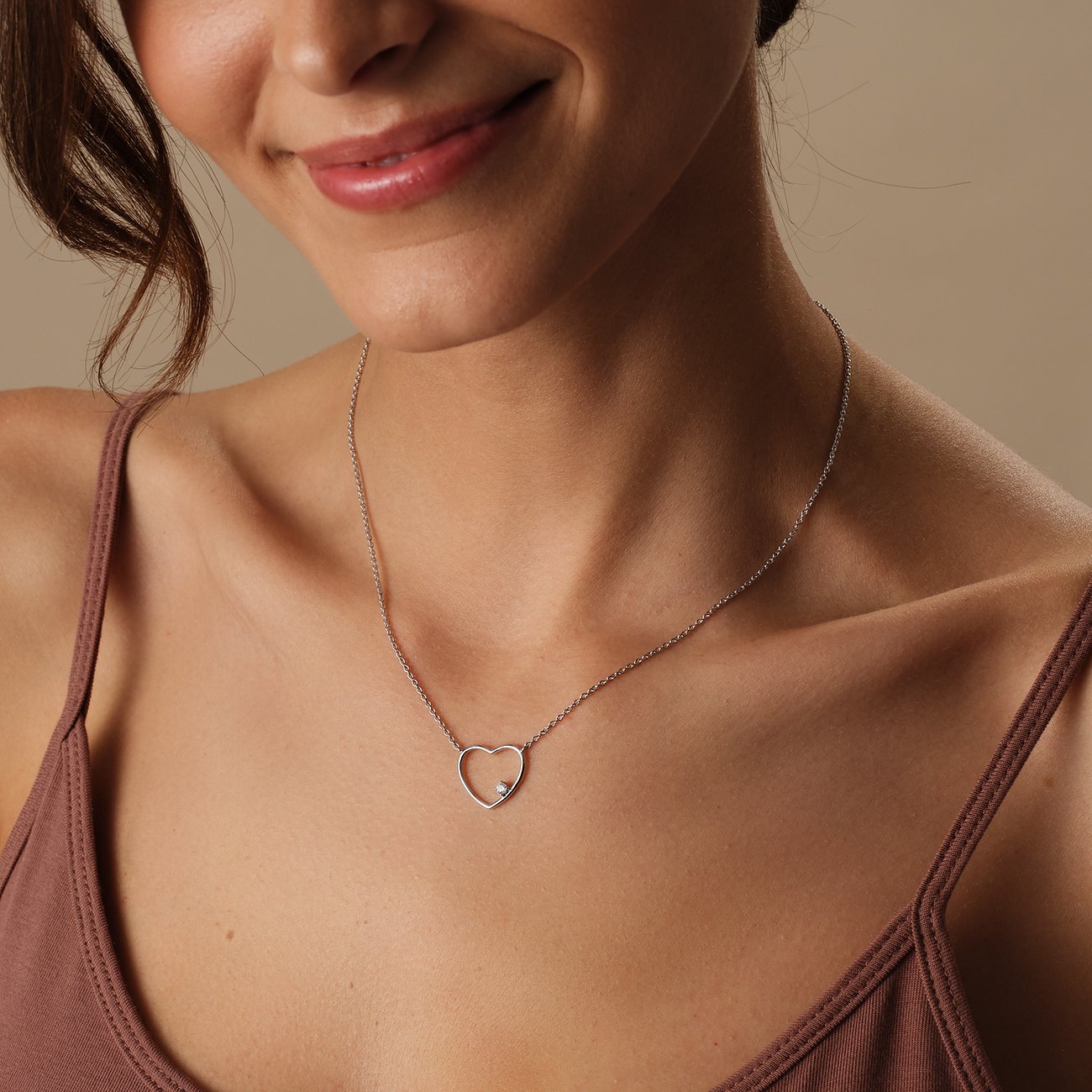 Een vrouw draagt een CHRIST ketting van gerecycled 925 zilver met hartvormige hanger en zirkonia als kleursteen.